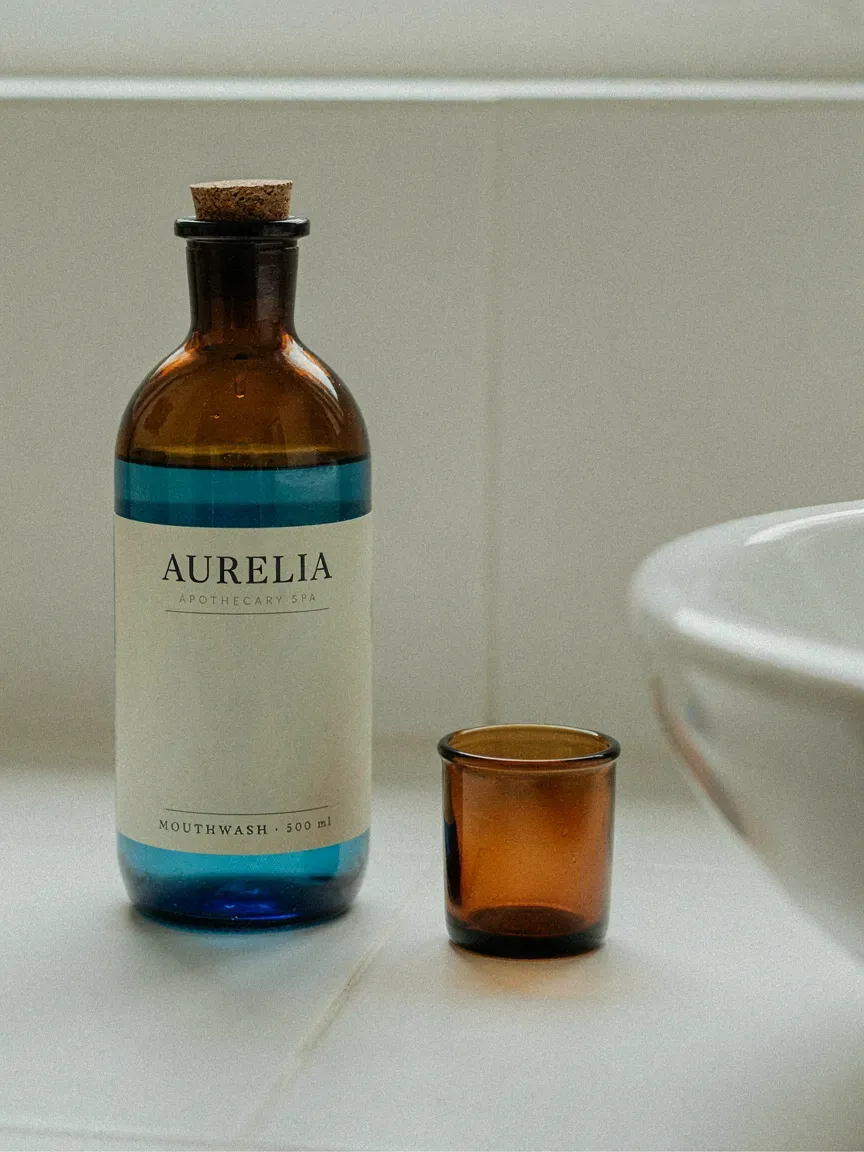 Dark amber glass bottle with cork and pour spout holding blue mouthwash on white counter