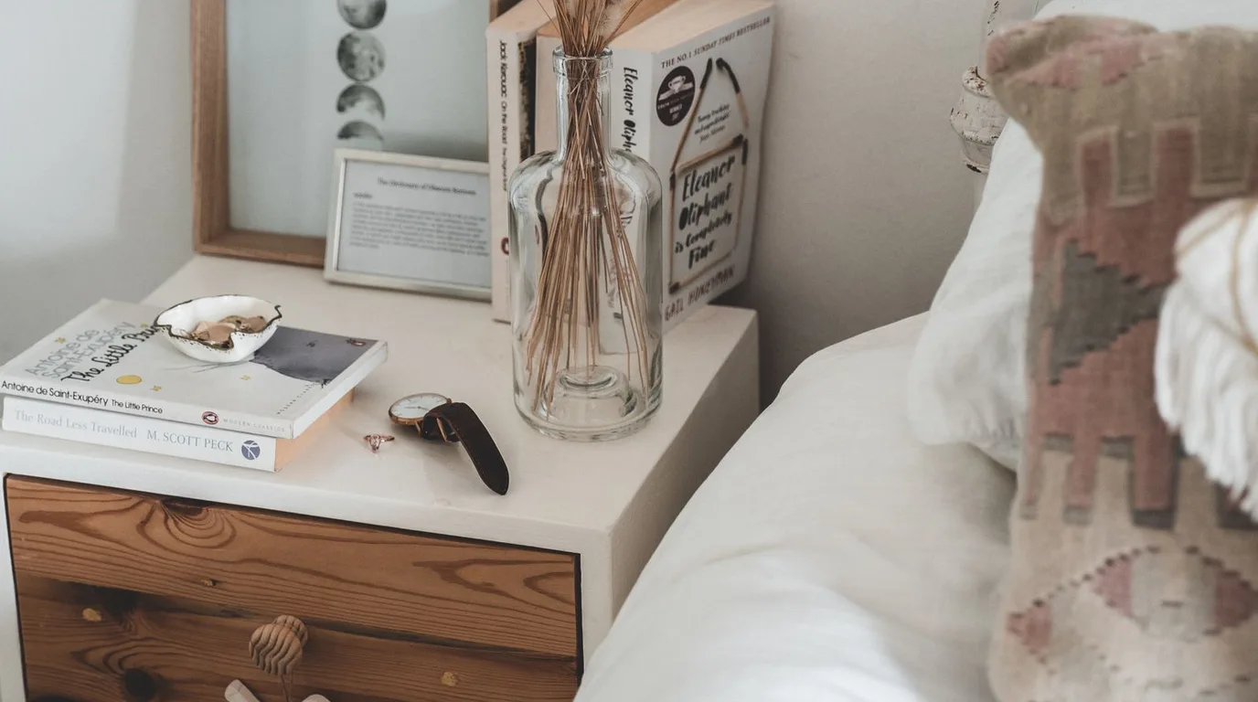 Bedside table styled with books, a glass vase, and dried flowers