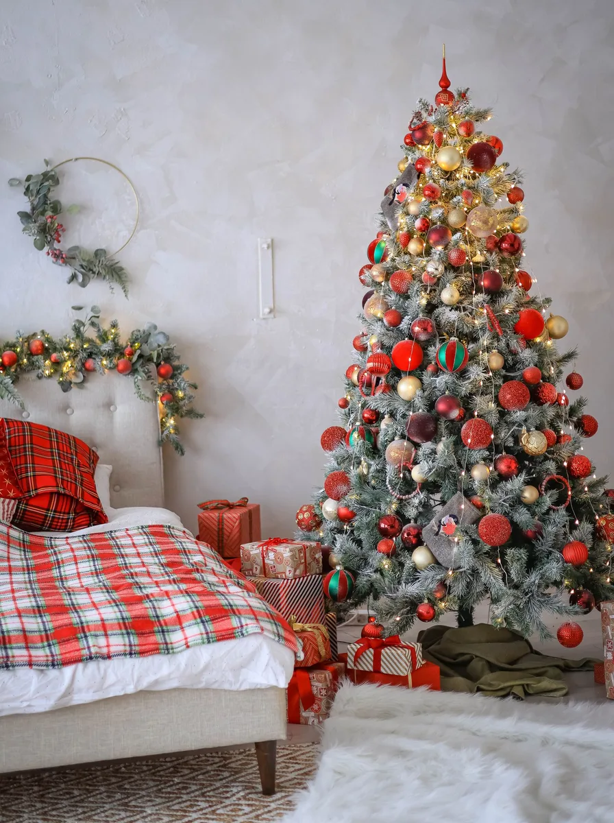 Bed with red plaid bedding beside a decorated Christmas tree