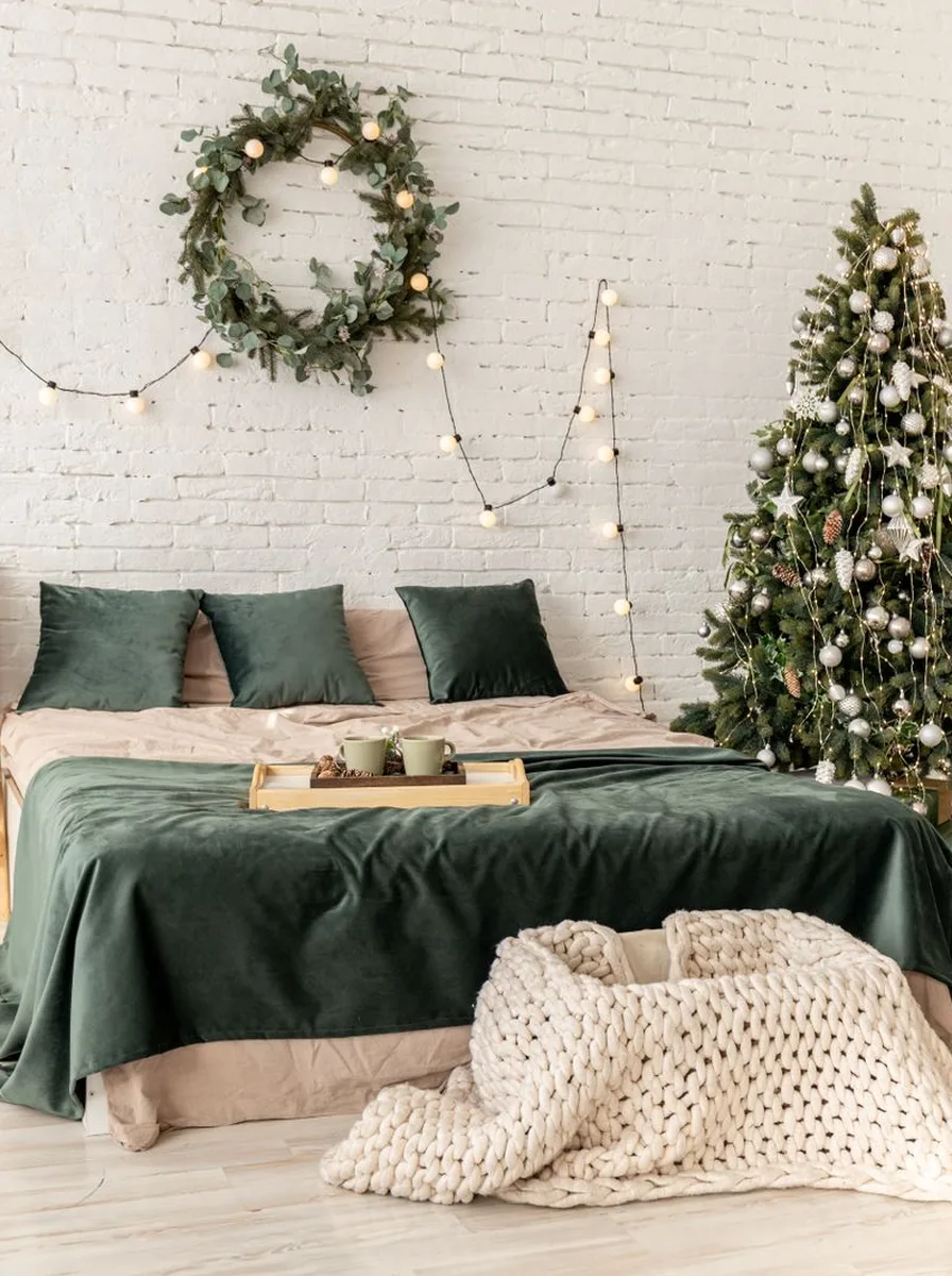 Bedroom with green bedding, wreath above the bed, and small Christmas tree