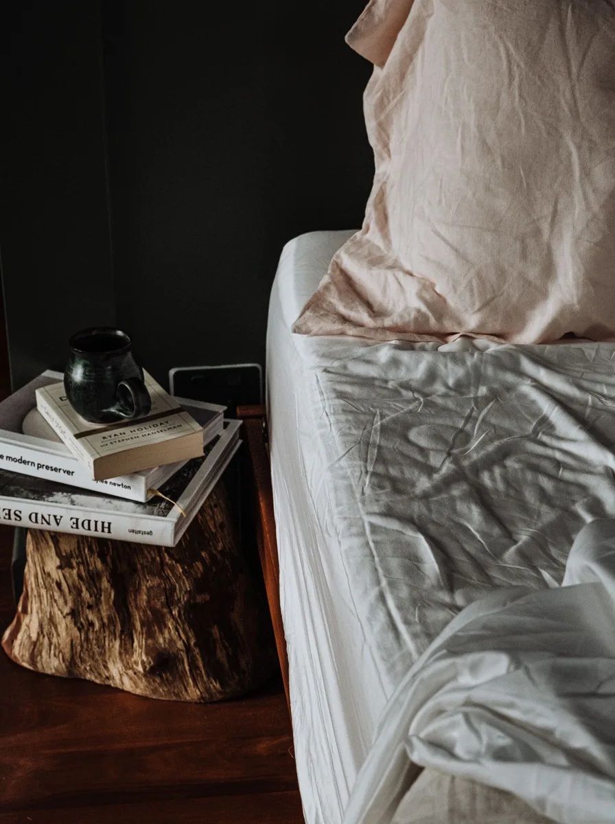 Bedside table styled with stacked books, a small plant, and warm light