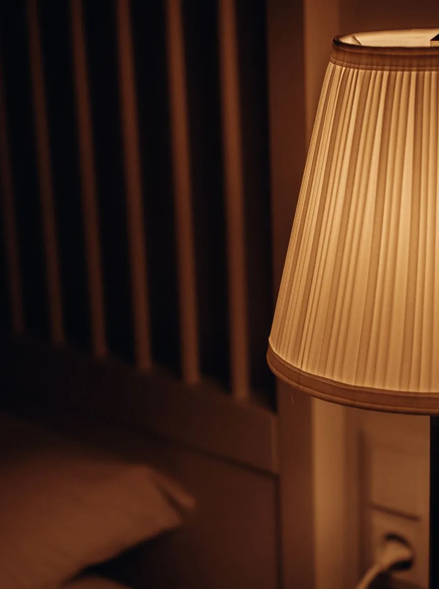 Pleated lampshade beside bed in dark room