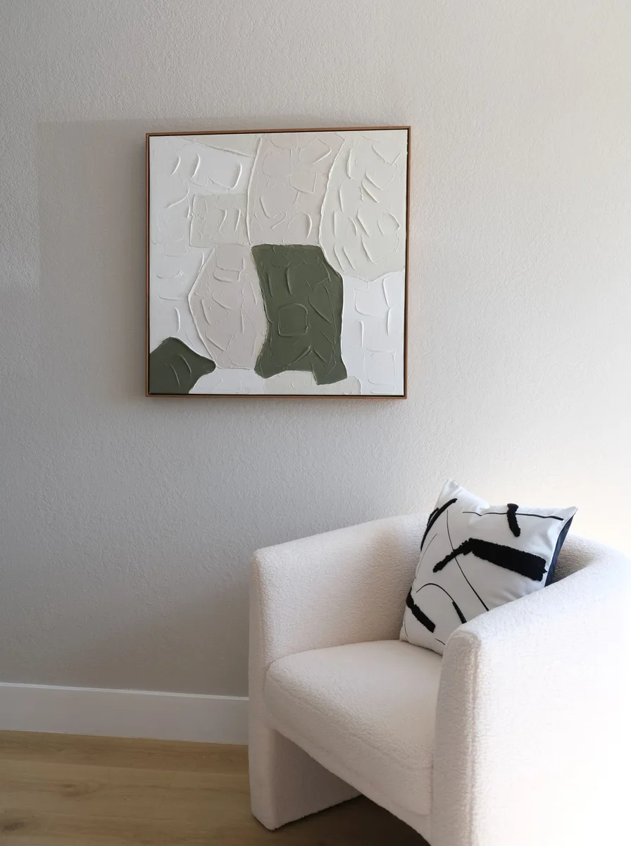 Sage green abstract canvas on a white wall beside a cream armchair