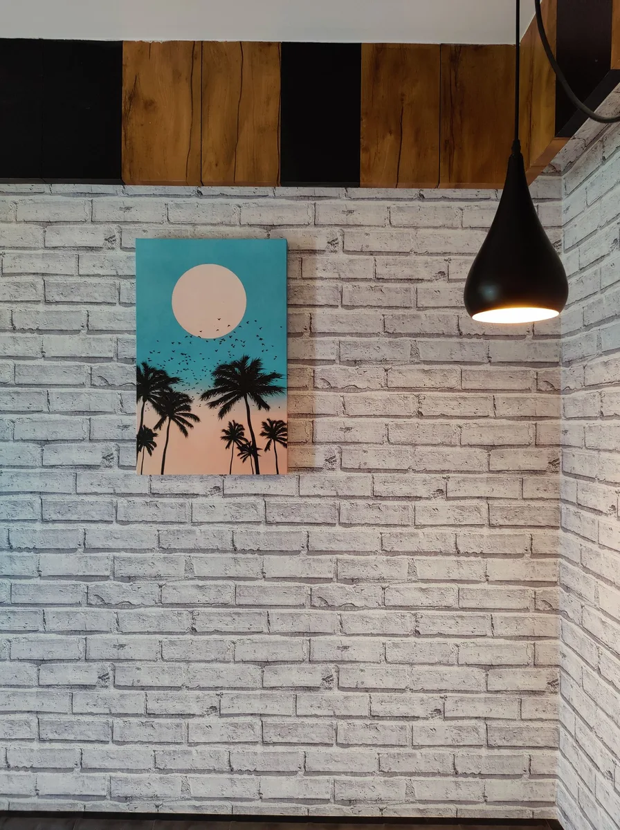 Small tropical palm sunset painting on a white brick wall beside a black pendant light