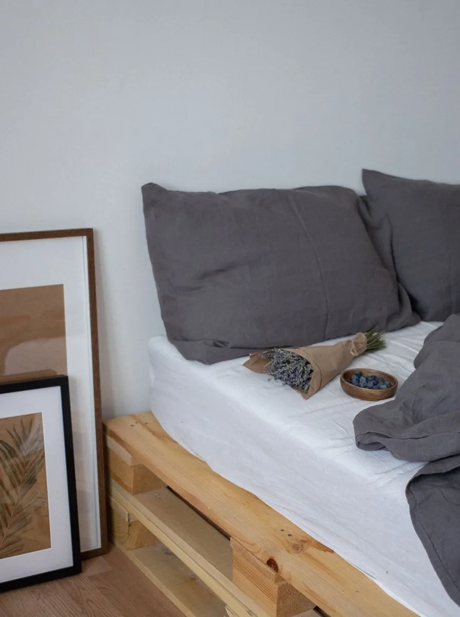 DIY pallet bed with grey linen pillows, dried lavender bouquet, and framed botanical prints