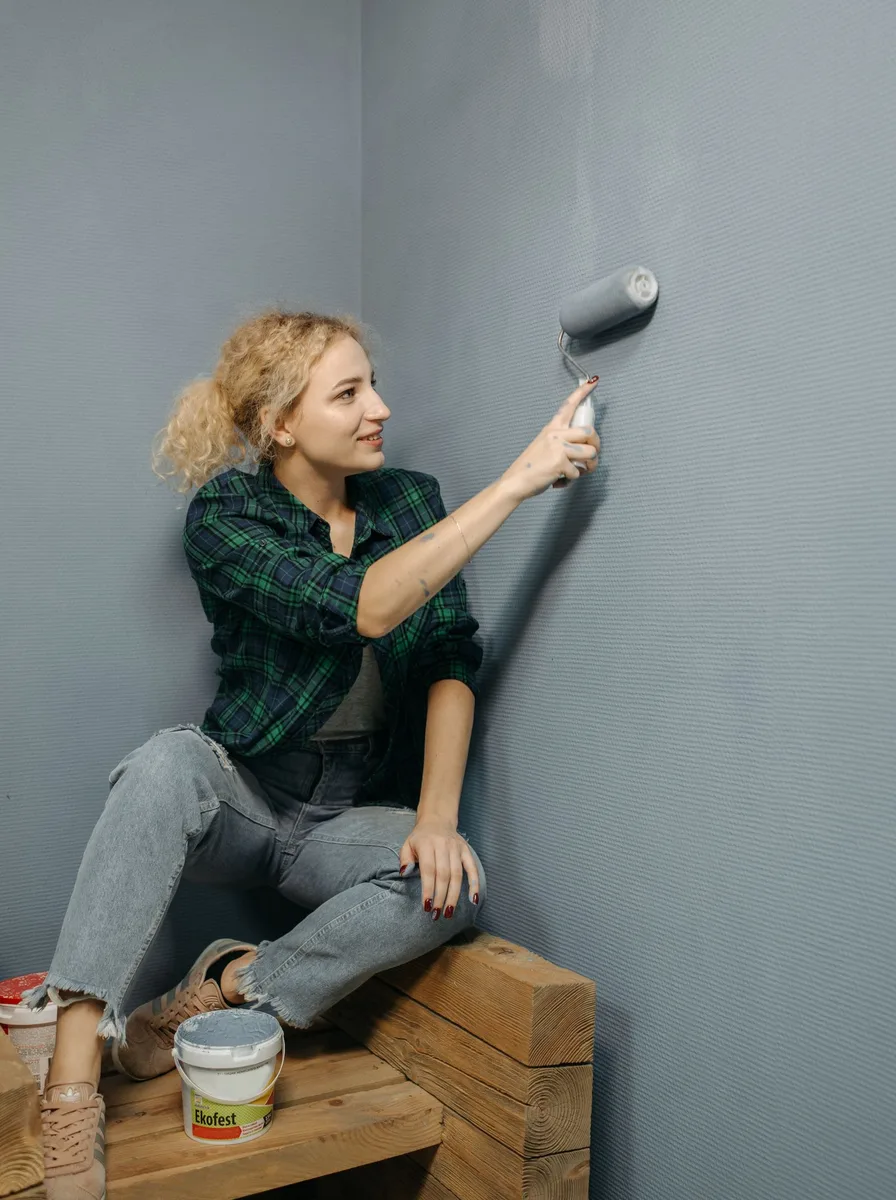 Woman painting her bedroom wall grey as an easy DIY project