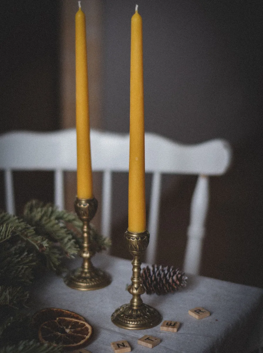 Gold-based hurricane lamp with a pillar candle beside an armchair and books in a reading nook