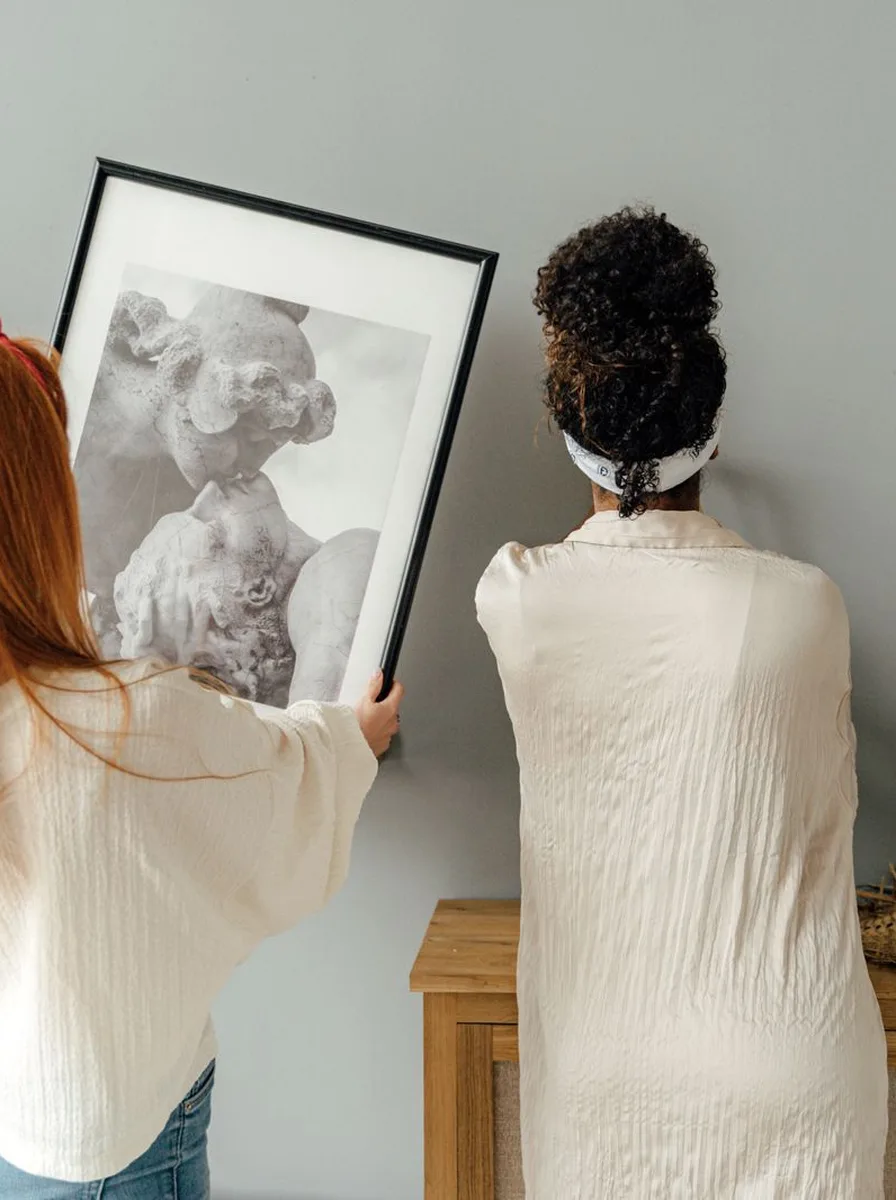 Two women hanging a large framed portrait on a wall