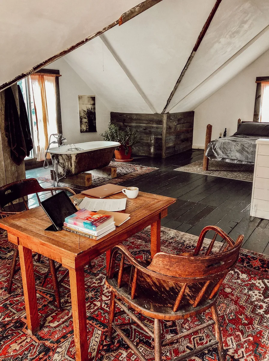 Rustic attic bedroom with a freestanding bathtub, wooden table, and dark wood floors
