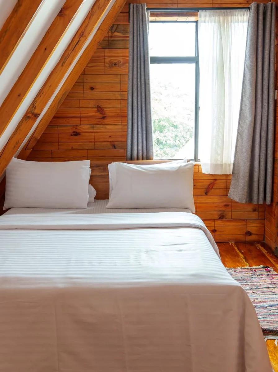 A-frame cabin bedroom with wood-paneled walls, white bedding, and grey curtains