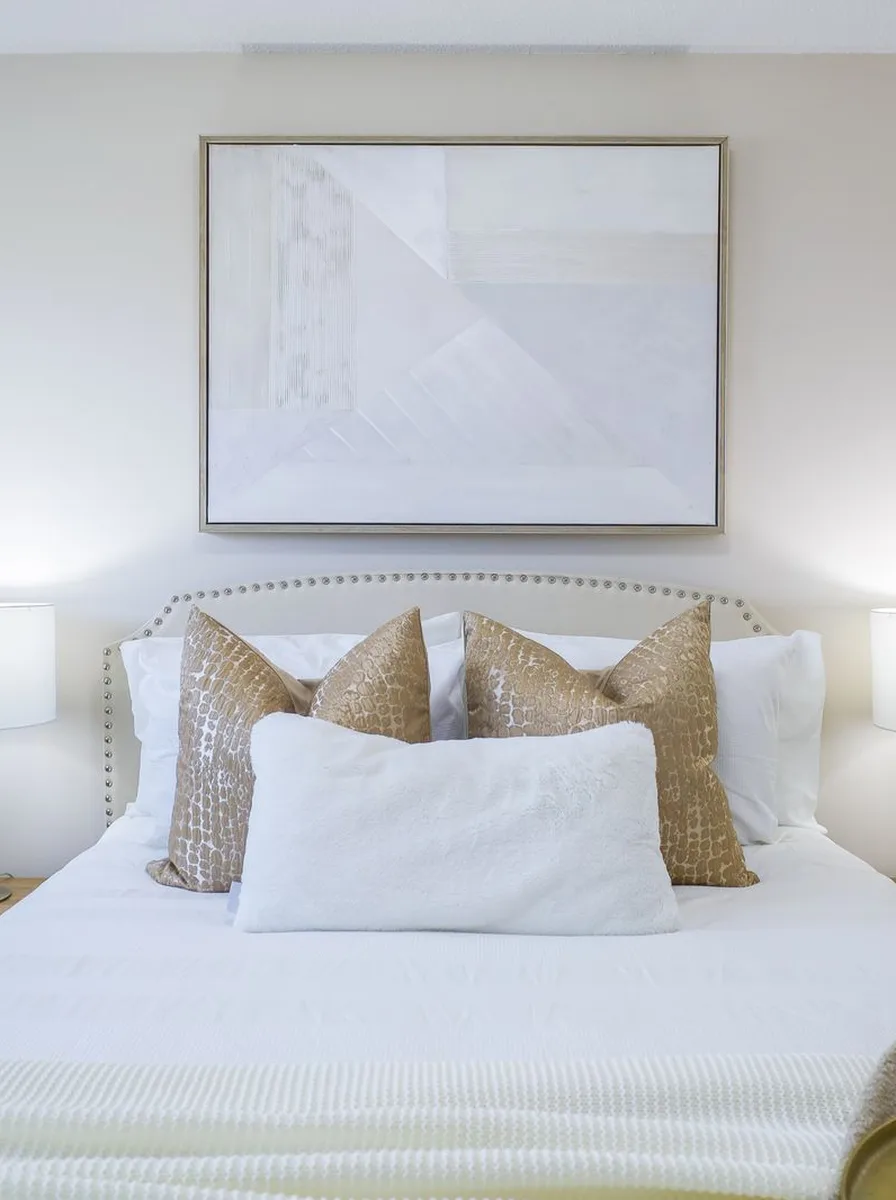 White bed with gold pillows and wall art