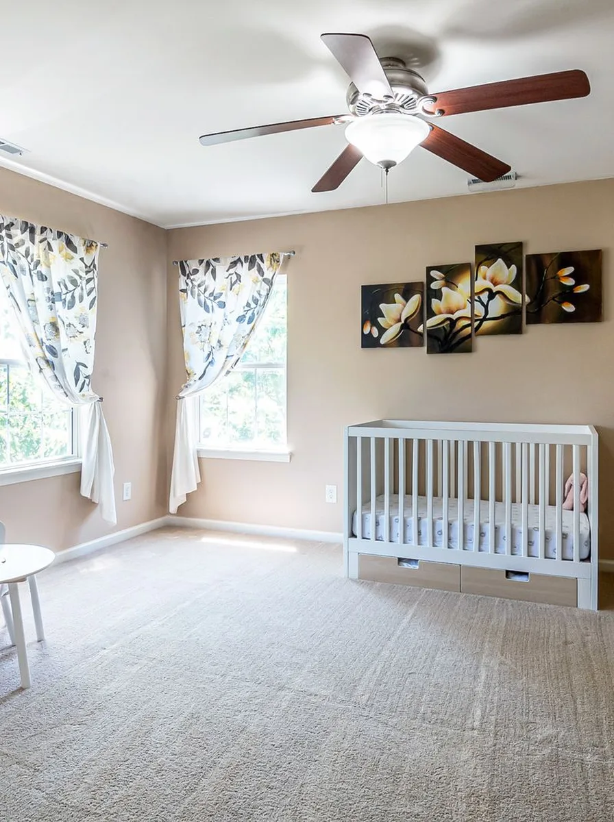 Neutral nursery with potted plant, sheer curtains, and warm lamp glow