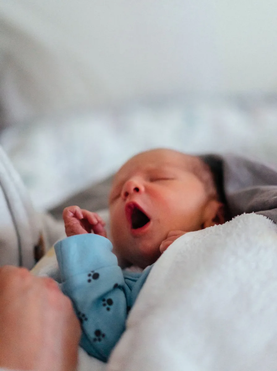 Yawning newborn baby wrapped in white