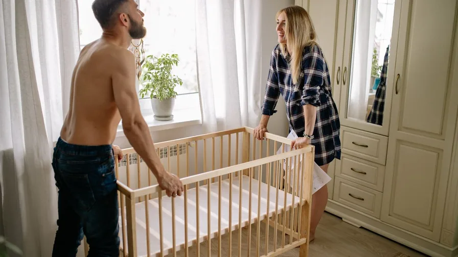 Parents assembling a crib in a neutral nursery