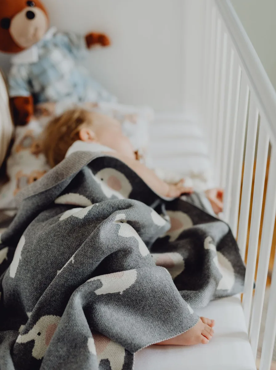 Sleeping baby in a crib with grey blanket
