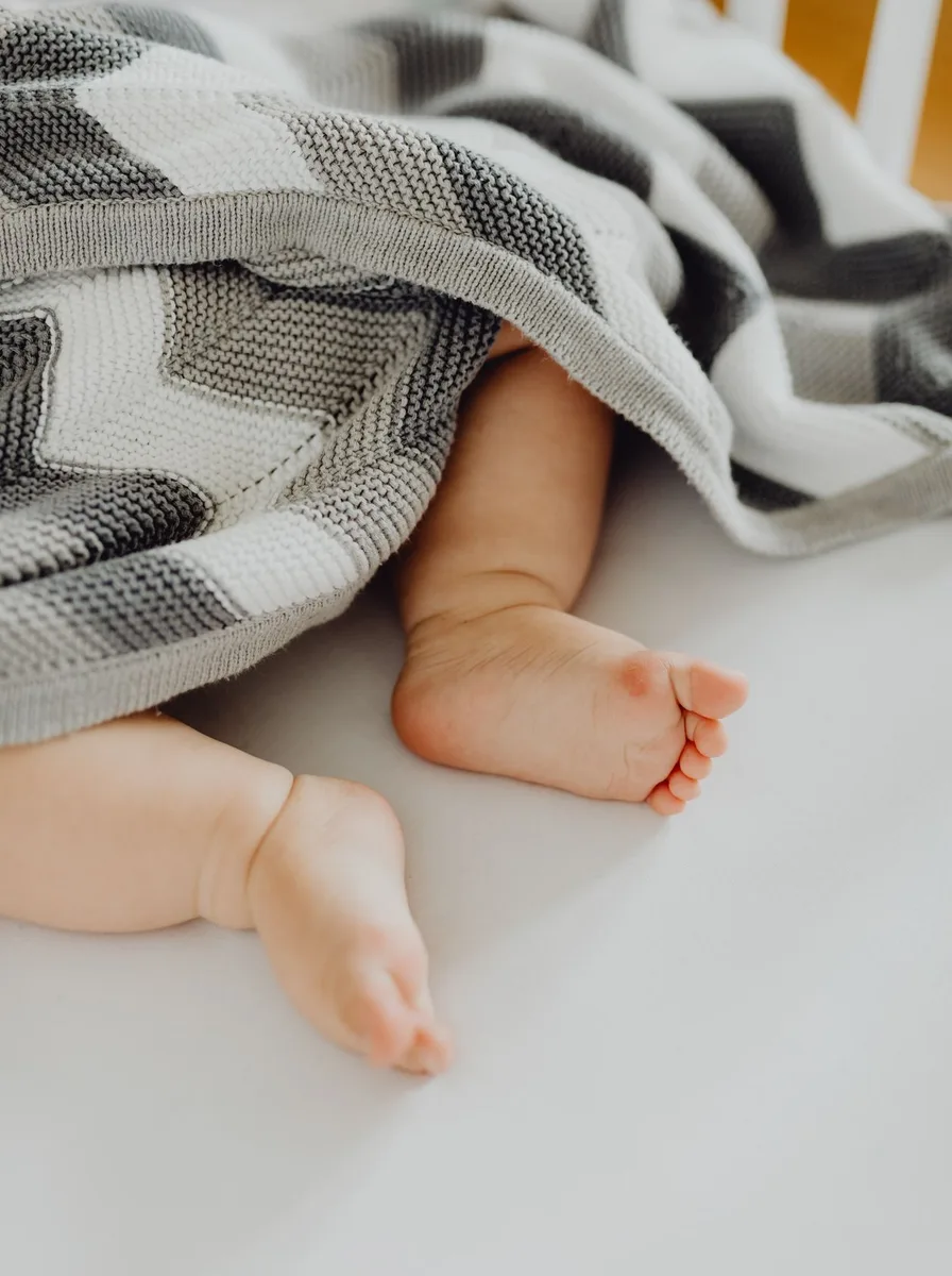 Baby legs under a grey striped blanket