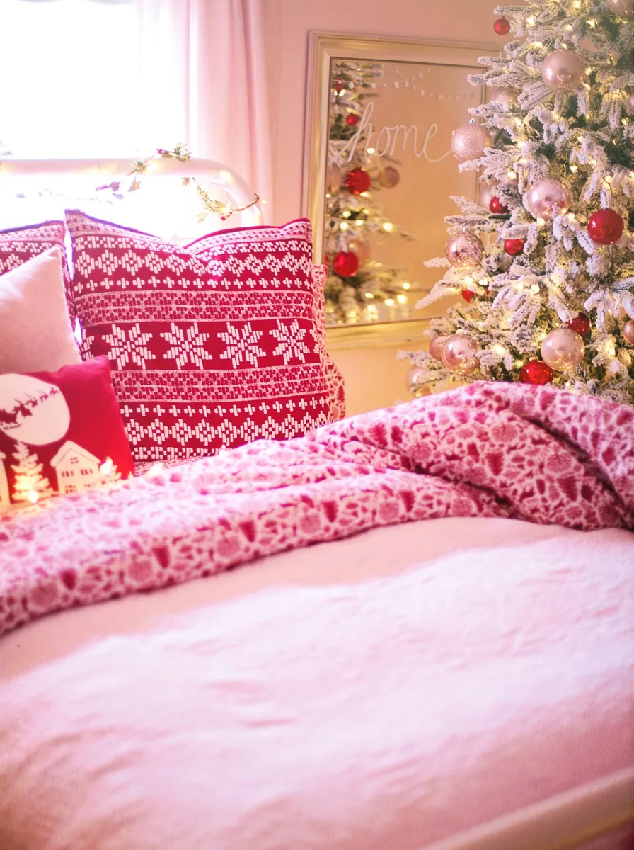 Pink bedding with Christmas pillows beside a lit tree