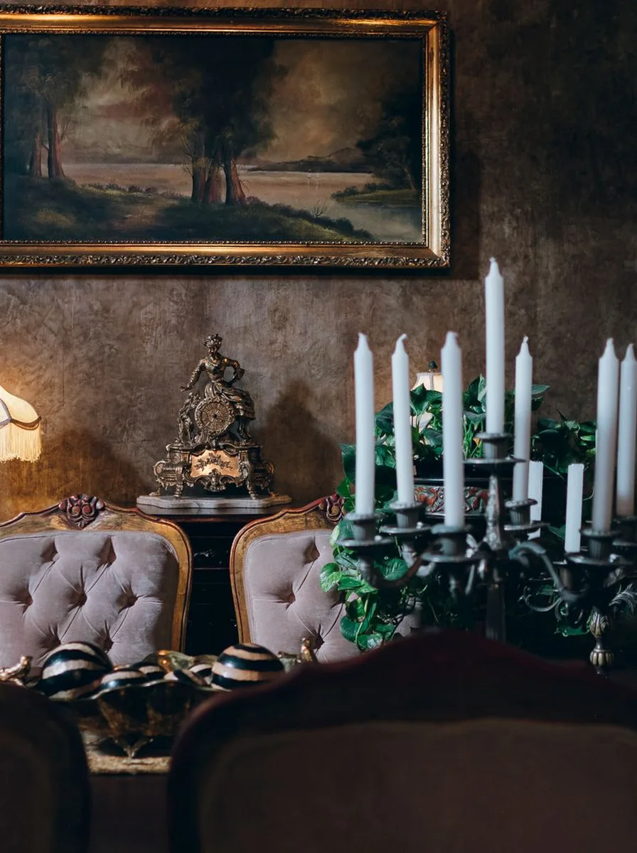 Dark dining wall with a gilt landscape painting and tall candelabra
