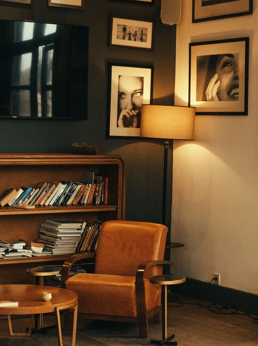 Moody reading corner with framed portrait photos on a dark green wall above a leather armchair