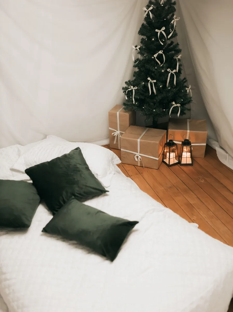 White bed with dark green pillows and a small Christmas tree
