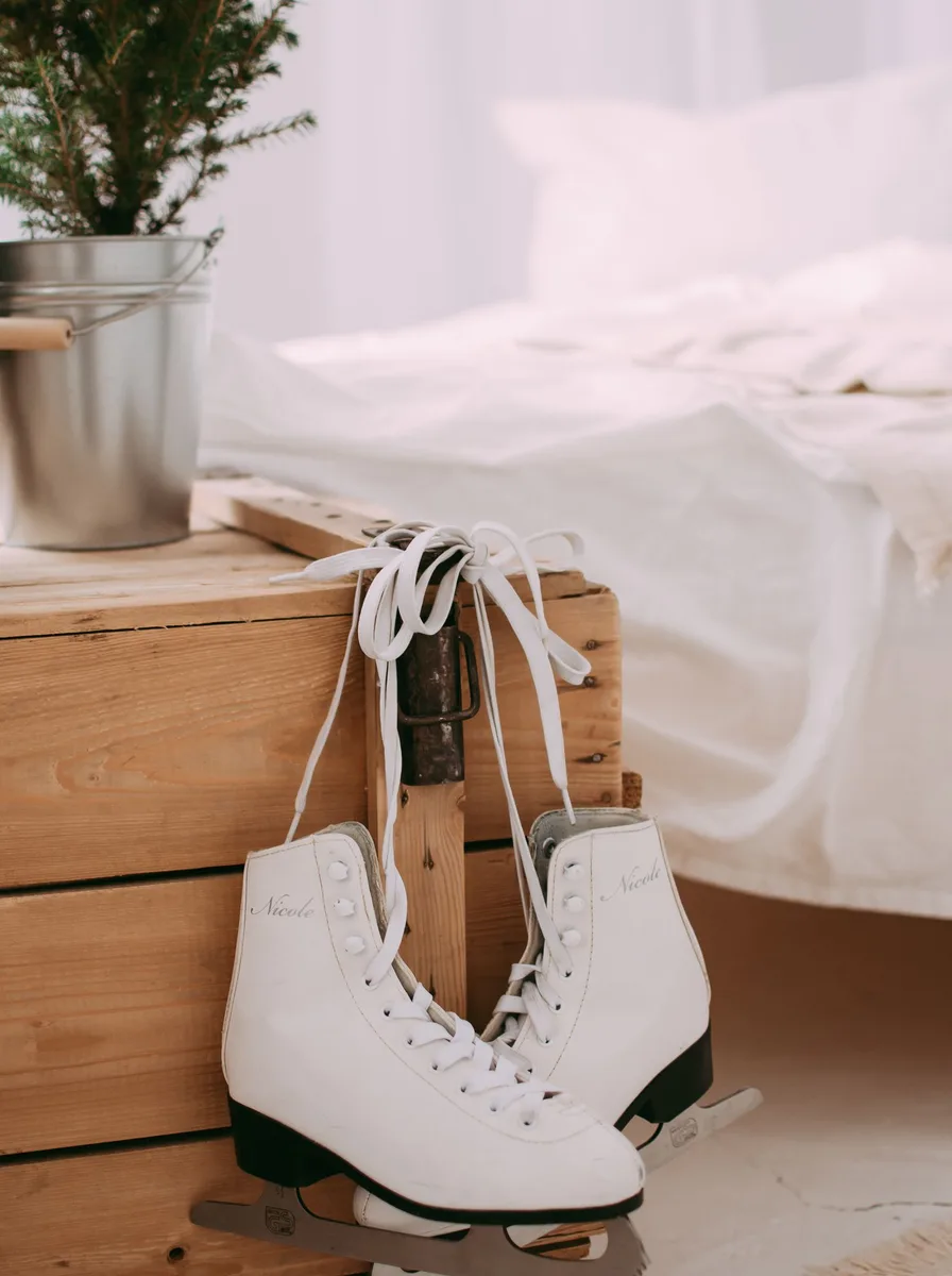 White ice skates on a wooden chest beside a bed